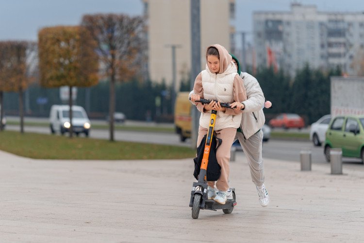 Двое молодых людей вдвоём едут на прокатном электросамокате (средстве индивидуальной мобильности)