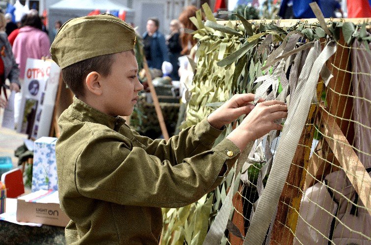 мальчик в солдатской форме плетёт маскировочную сеть