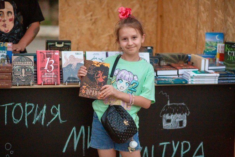 Девочка с книгой в руках в павильоне книжного магазина "Чарли" на фестивале "Александровская крепость" в Усть-Лабинске