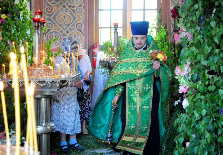 настоятель храма святого князя Владимира в хуторе Аргатове иерей Григорий Гуреев с украшенным цветами распятием в левой руке и кадилом в правой, в украшенном зеленью храме