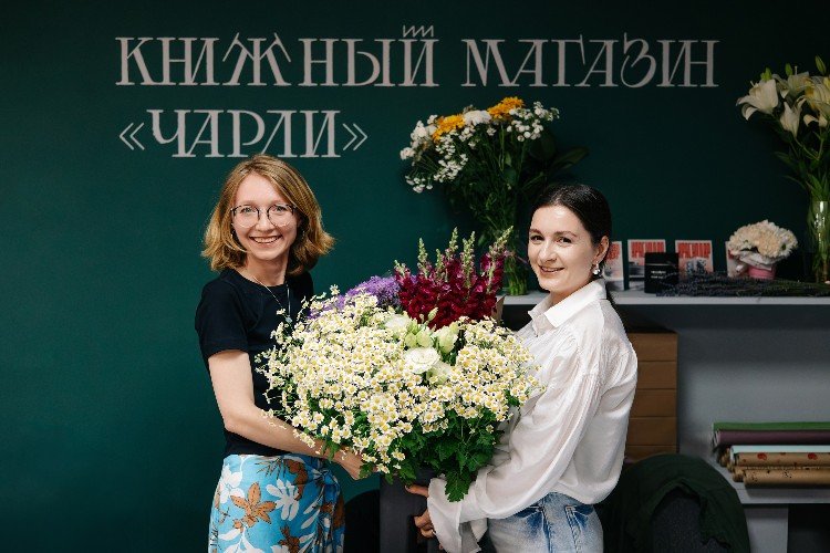 две девушки с большим букетом полевых цветов на фоне вывески книжного магазина "Чарли"