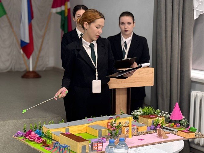 школьница показывает макет с постройками и озеленением