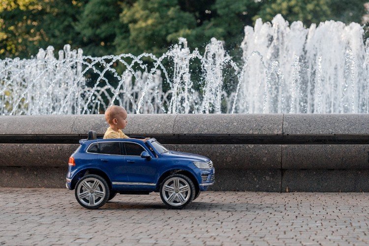 Малыш едет в детском автомобиле возле фонтана