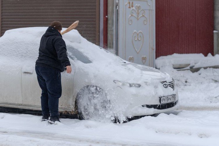Мужчина чистит машину от снега