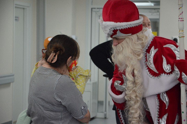 Девочка на руках у мамы общается с Дедом Морозом