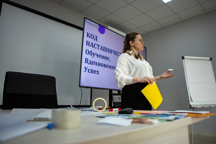 Юлия Полубенко, ведущий специалист отдела обучения и развития персонала ГК «Прогресс Агро», с жёлтым листом бумаги в руках стоит у маркерной доски