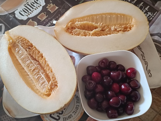 разрезанная пополам дыня и черешня в блюдце