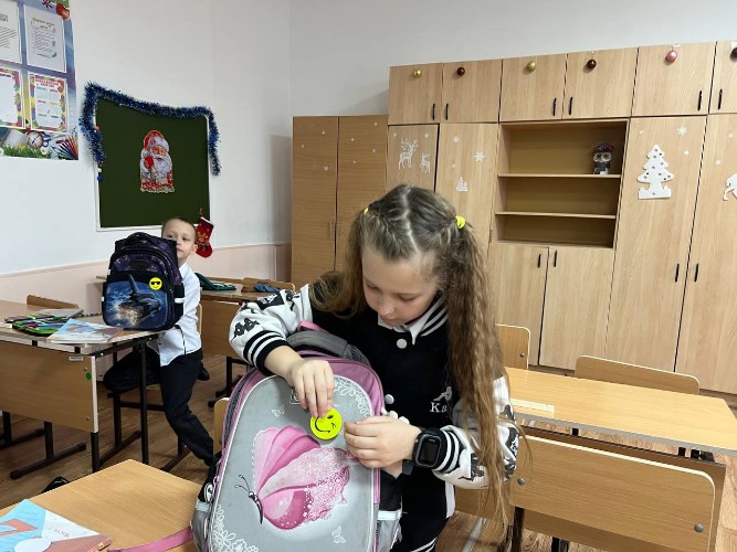 Девочка клеит на рюкзак световозвращающий значок